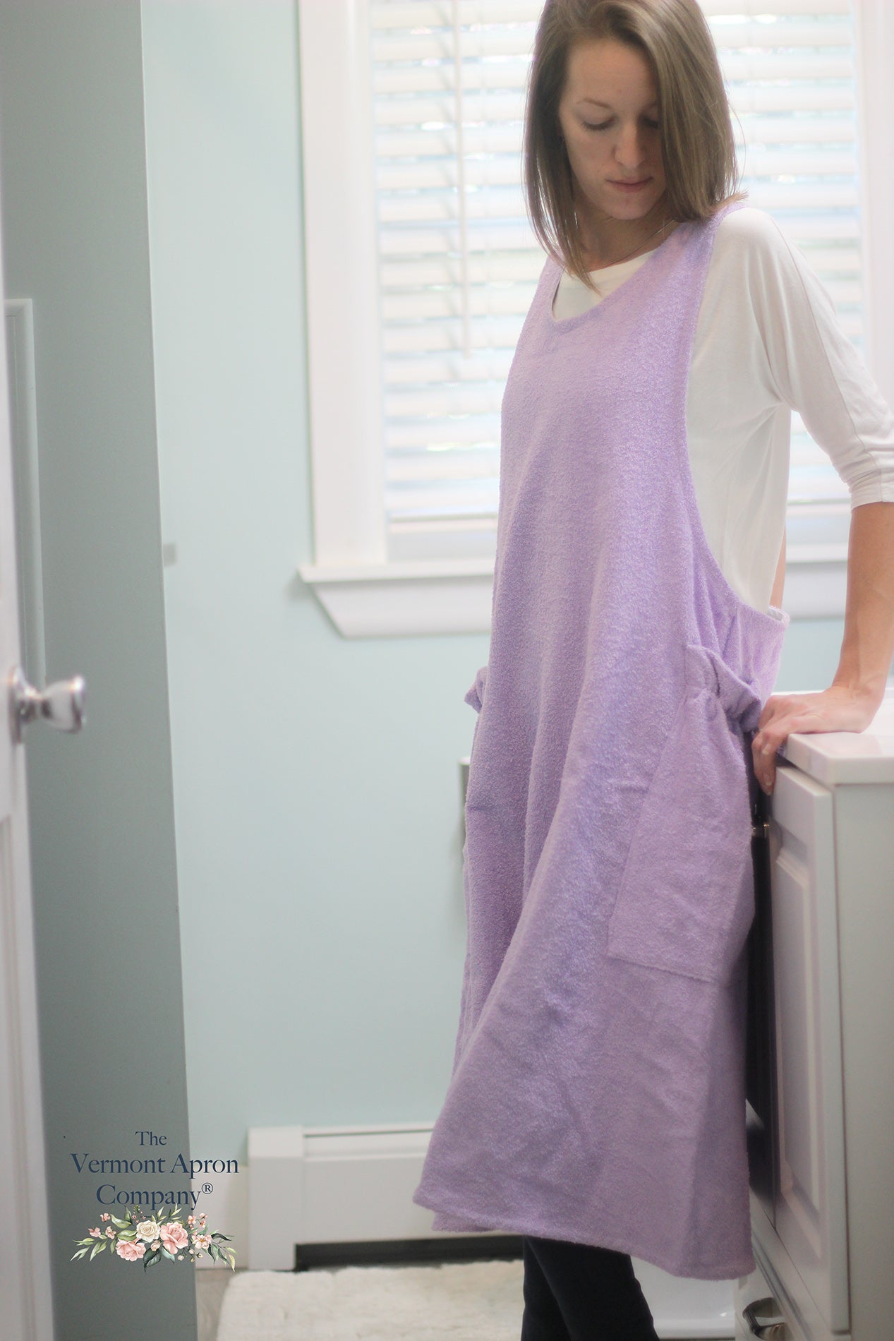 XS-5X Lilac Terry Apron - No Tie Crossback Apron - The model is near the bathtub showing a side view of the apron.