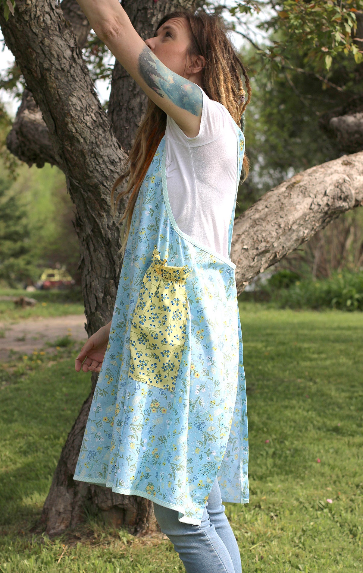 No Tie Apron in Blue Floral with Yellow Pockets - Side view with model reaching up into a tree.