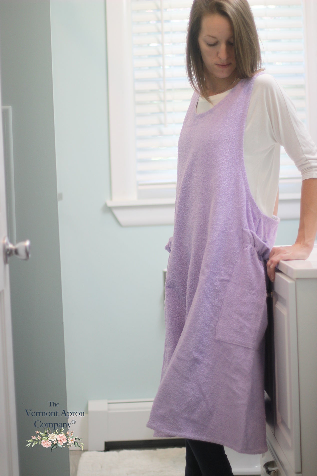 XS-5X Lilac Terry Apron - No Tie Crossback Apron - The model is  near the bathtub showing a side view of the apron.